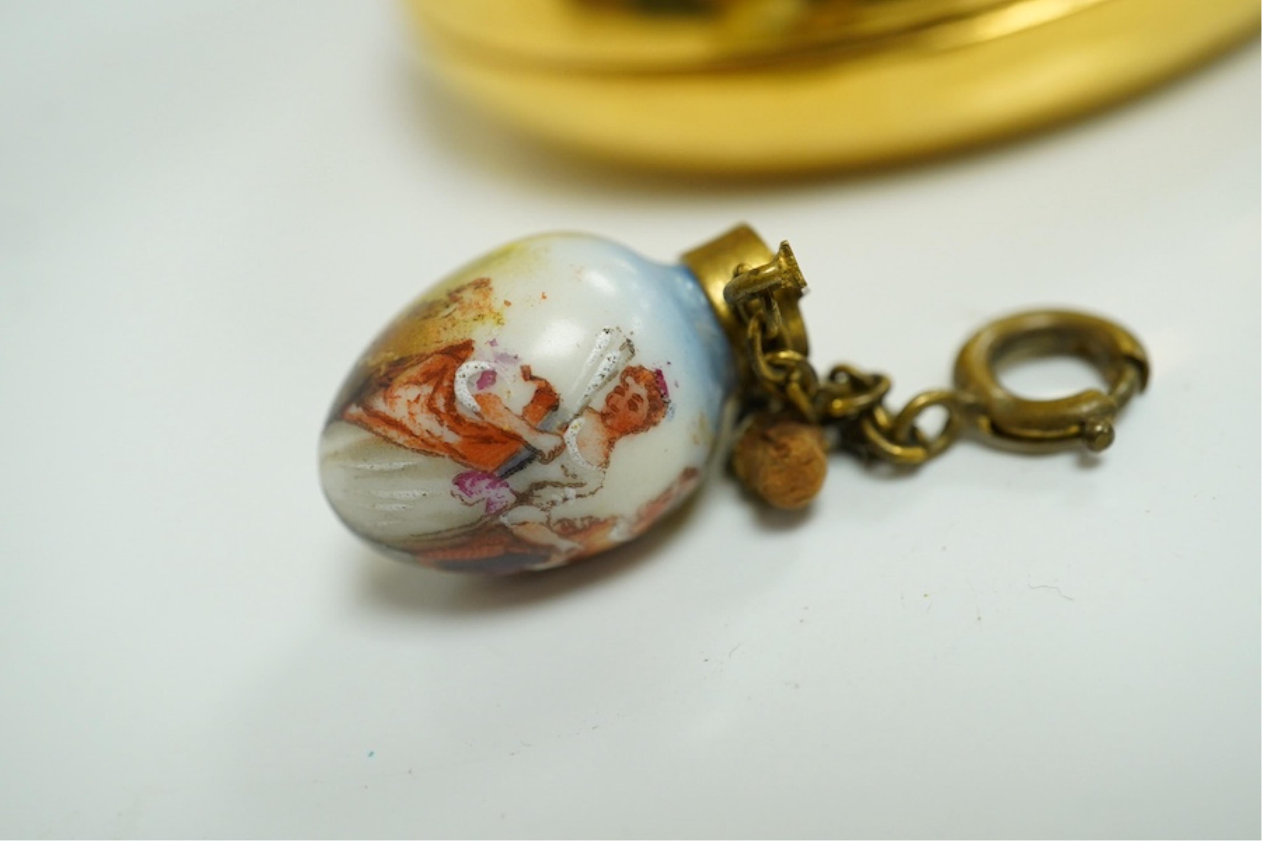 A miniature porcelain egg shaped scent bottle, on chain, two Halcyon Days scent bottles and a circular enamelled paperweight, (4). Condition - fair